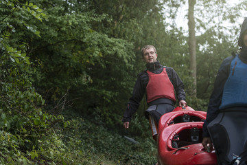 Athletes carry a sports boat with a kayak along a forest path to the river.
