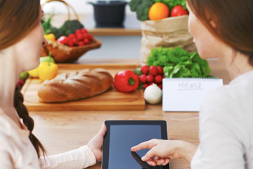 Woman cooks at the kitchen using tablet computer. Copy space area at touch pad. Healthy meal, vegetarian food and lifestyle concepts