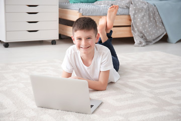 Happy boy with laptop lying on cozy carpet at home