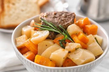 Bowl with tasty meat and potatoes on table