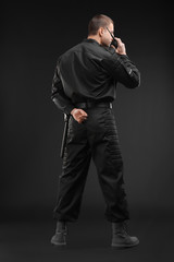Male security guard using portable radio transmitter on dark background