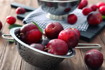Colander with ripe juicy plums on table