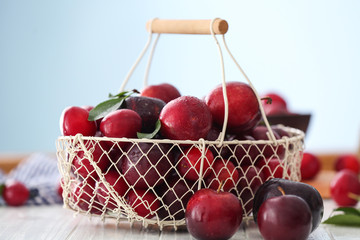 Metal basket with ripe juicy plums on table