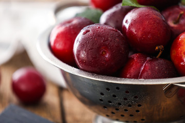 Colander with ripe juicy plums on table, closeup