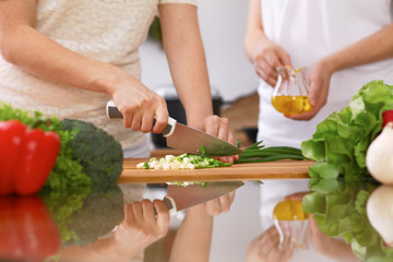 Closeup of human hands cooking in kitchen. Mother and daughter or two female friends cutting vegetables for fresh salad. Healthy meal, vegetarian food and lifestyle concepts