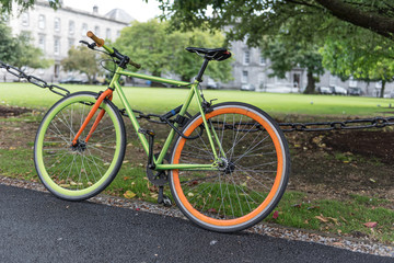 Fototapeta na wymiar Colourful, green and orange bicycle locked to a chain-link fence in the grounds of the university in Dublin, Republic of Ireland.