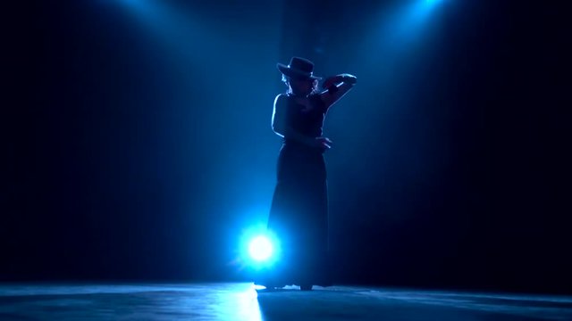 Girl is dancing with castanets in her hands dancing. Llight from behind. Dark background. Silhouette