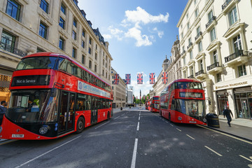 Plakat LONDON, ENGLAND - JULY 3, 2016. Regent Street at sunny day with British flags and four red buses