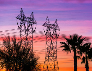 Silhouette of high voltage lines and transmission towers thru the desert at sunset.