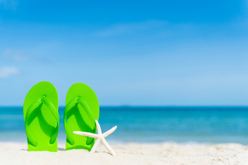 green flip flop with starfish on sandy beach, green sea and blue sky background for summer holiday...