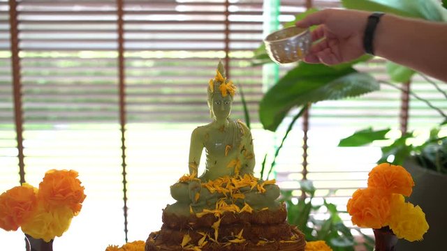 Buddhist Songkran. The Thai new year. Mens hand pours a Buddha statue with water and jasmine petals