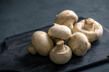 White champignons on the dark kitchen table. Cooking delicious dishes with mushrooms