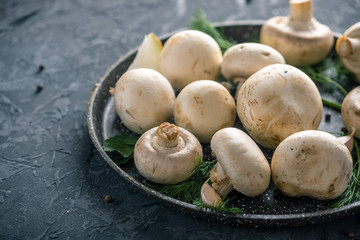 White Champions on the pan and ingredients on the dark kitchen table. Concept of cooking mushroom dishes. Close up