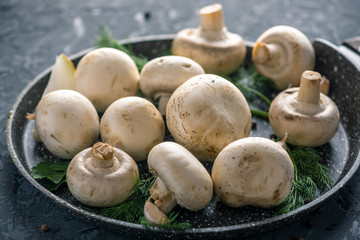 White Champions on the pan and ingredients on the dark kitchen table. Concept of cooking mushroom dishes. Close up
