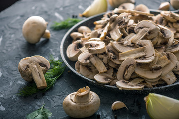 White fresh sliced champignons in a pan on the dark kitchen table. Concept of cooking mushroom...