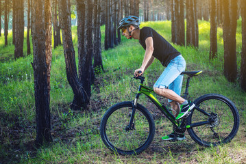 Obraz premium Man in a helmet riding on a green mountain bike in the woods. Cyclist in motion. Concept of active and healthy lifestyle