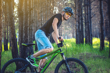 Obraz premium Man in a helmet riding on a green mountain bike in the woods. Cyclist in motion. Concept of active and healthy lifestyle