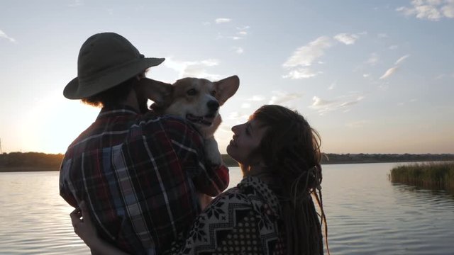 happy young couple play with corgi dog on the river beach against the sunset 
