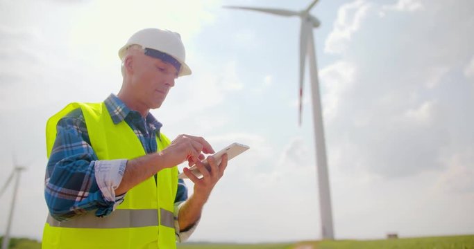 Engineer Using Digital Tablet At Wind Turbine Farm Against Sky