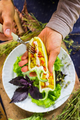 Woman hands holds and tastes with fork green raw bell peppers stuffed with quinoa, bulgur, tomato, basil leaves and other vegetables for lunch or dinner. Vegan vegetarian healthy food.