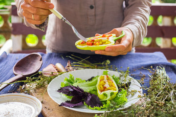 Woman hands holds and tastes with fork green raw bell peppers stuffed with quinoa, bulgur, tomato, basil leaves and other vegetables for lunch or dinner. Vegan vegetarian healthy food.