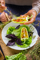 Woman hands holds and tastes with fork green raw bell peppers stuffed with quinoa, bulgur, tomato, basil leaves and other vegetables for lunch or dinner. Vegan vegetarian healthy food.