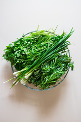 A bunch of greens and herbs. Green onion sprouts, cilantro, tarragon in glass bowl.
