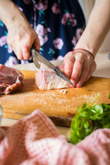 Woman hands cuts raw red meat into pieces with sharp knife on wooden board.