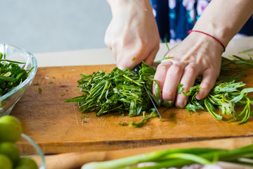 Fototapeta na wymiar Woman hands cuts fresh herbs on wooden board preparing salad or lunch and dinner. Raw vegan vegetarian healthy food. 
