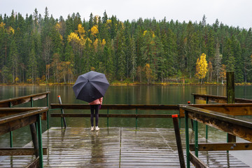 Girl holding umbrella standing on pier in rainy day in Vimmerby, Sweden. Selective focus