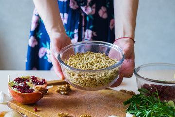 Woman hands holds grated, mixed and cut walnuts in glass bowl. Ingredient for Georgian traditional appetizer food - pkhali. Preparation process with garlic, pomegranate, cilantro, onion.