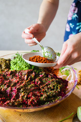 Woman hands adds adjika (ajika) and preparing ingredients for pkhali balls - traditional Georgian food with walnuts beetroot and spinach.