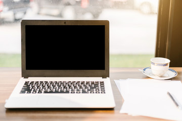Fototapeta premium Mockup image of laptop with blank black screen,smart phone and document on wooden table of In the coffee shop.