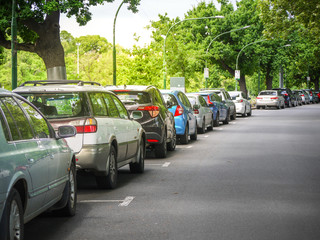 Many cars parked and lined up under trees on urban street. City of Melbourne, VIC Australia.