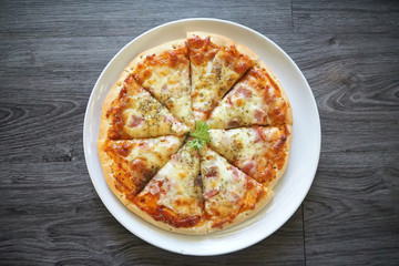 Pizza ham and grilled mozzarella cheeses decorate on top with coriander on white dish with gray wooden ready to serve