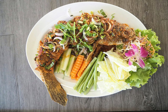 Fried snakefish pour with hot and spicy thai herb sauce decorate with vegetables on white dish ready for serve