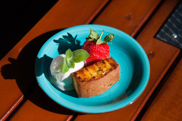 Strawberries with ice cream and biscuits on a blue plate standing on a wooden table