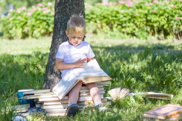 little prodigy boy is reading big book in garden. staircase and steps of books - education, knowledge, and people concept