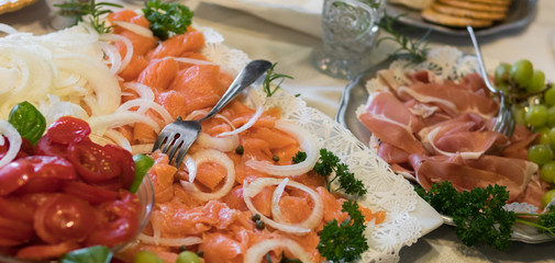 Gourmet platter of smoked salmon, tomatoes, onions, calipers, prosciutto, and grapes.