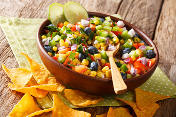 Delicious food: salsa from corn, blueberries, pepper, herbs and onions close-up in a bowl and nachos chips. horizontal
