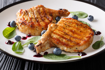 Delicious grilled pork fillet steak with rib served with blueberry sauce and baby spinach closeup on a plate on a wooden table. horizontal