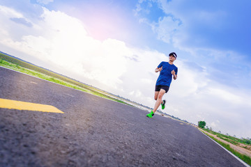 Obraz premium Young man jogging along the road. with cloudy sky as background