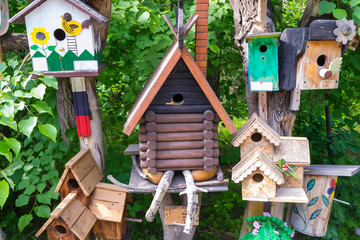 A wooden birdhouse in which the birds live, with green roof and cone against the background of green leaves
