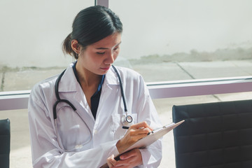 Asian doctor sitting on clipboard writing In the hallway of the hospital