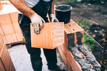 bricklayer moving bricks and building outside brick walls on construction site