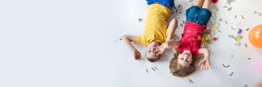 A girl and a boy lay on the white floor and play colorful air balloons on the birthday party top view
