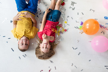 A girl and a boys lay on the white floor and play colorful air balloons on the birthday party