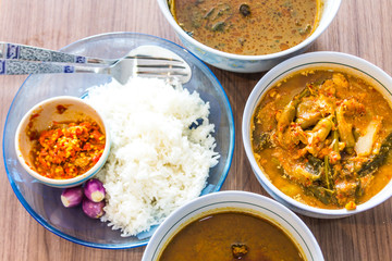 Top view of pure white jasmine rice in blue plate Have a cup of red chili paste. And there are three folk red curry paste on a brown wooden table.
