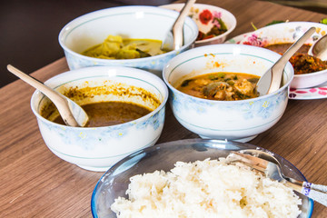 Side view inside the bedroom Pure white jasmine rice in blue plate Have a cup of red chili paste. And there are three folk red curry paste on a brown wooden table.