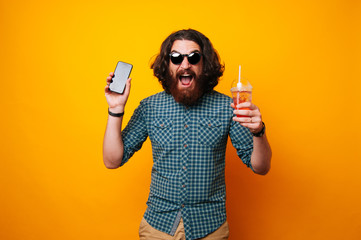 Amazed bearded man holding a phone and juice drink